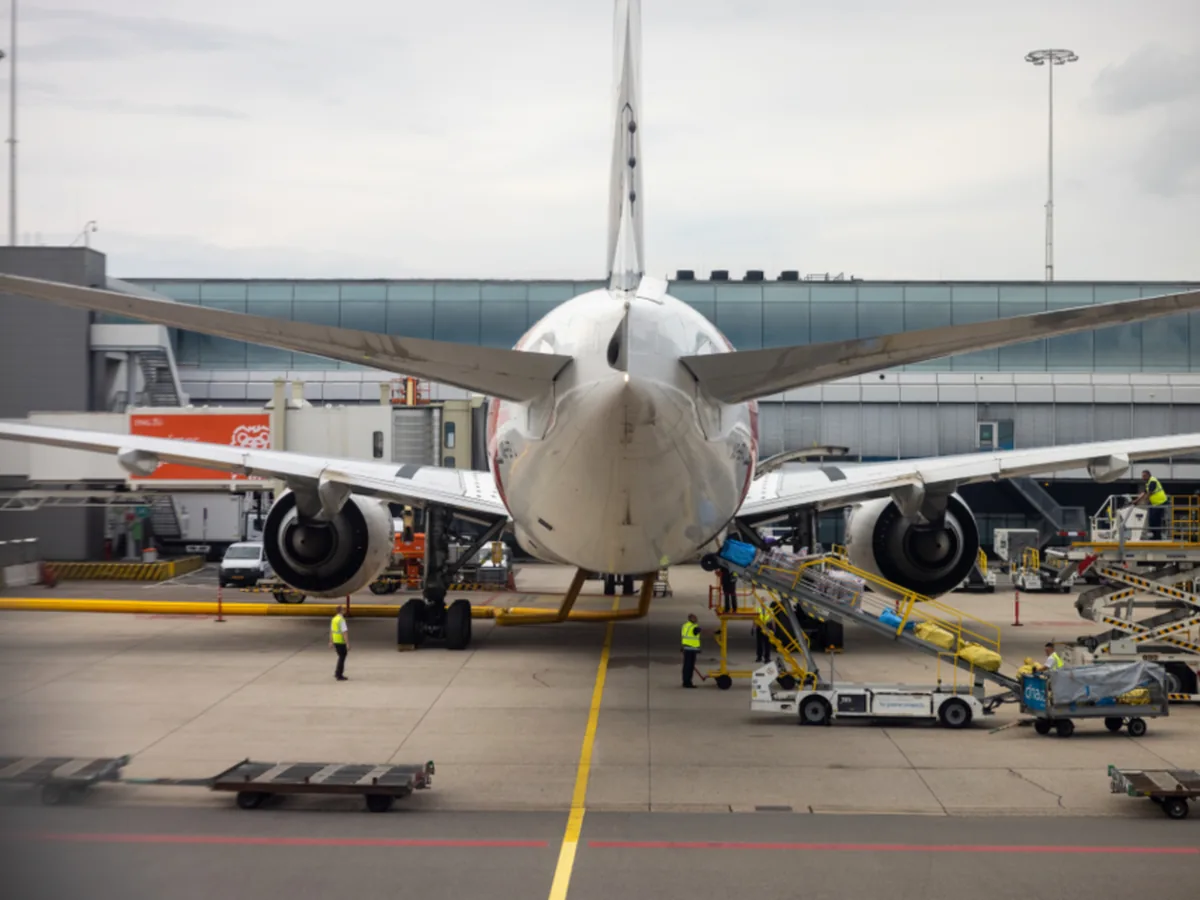 A passenger jet parked at an airport stand while ground crew service it.