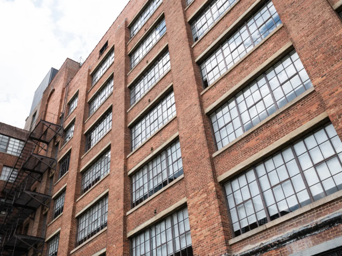 A brick industrial building with rows of large steel-framed windows.