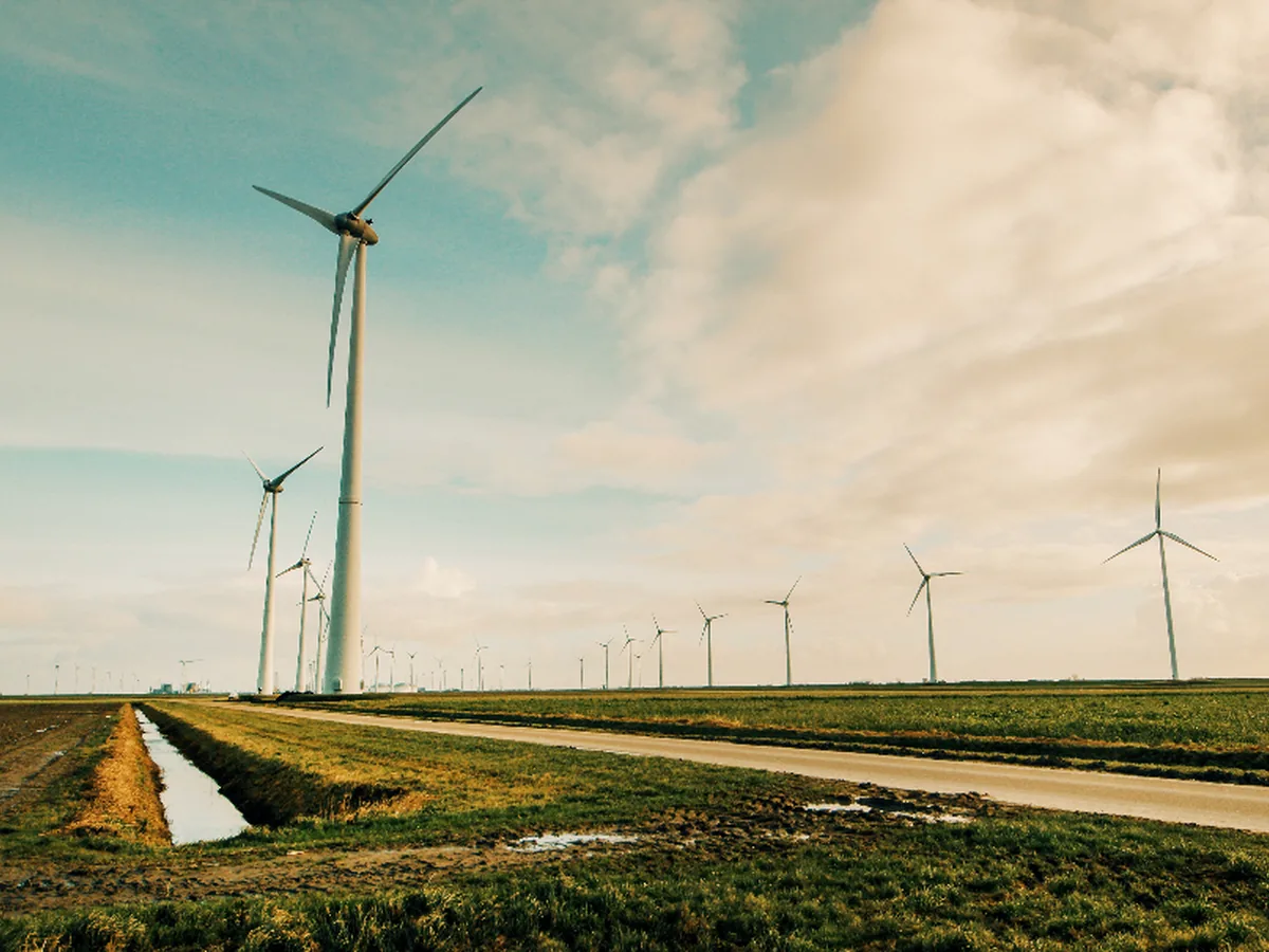Wind turbines standing in flat farmland beside a drainage channel.