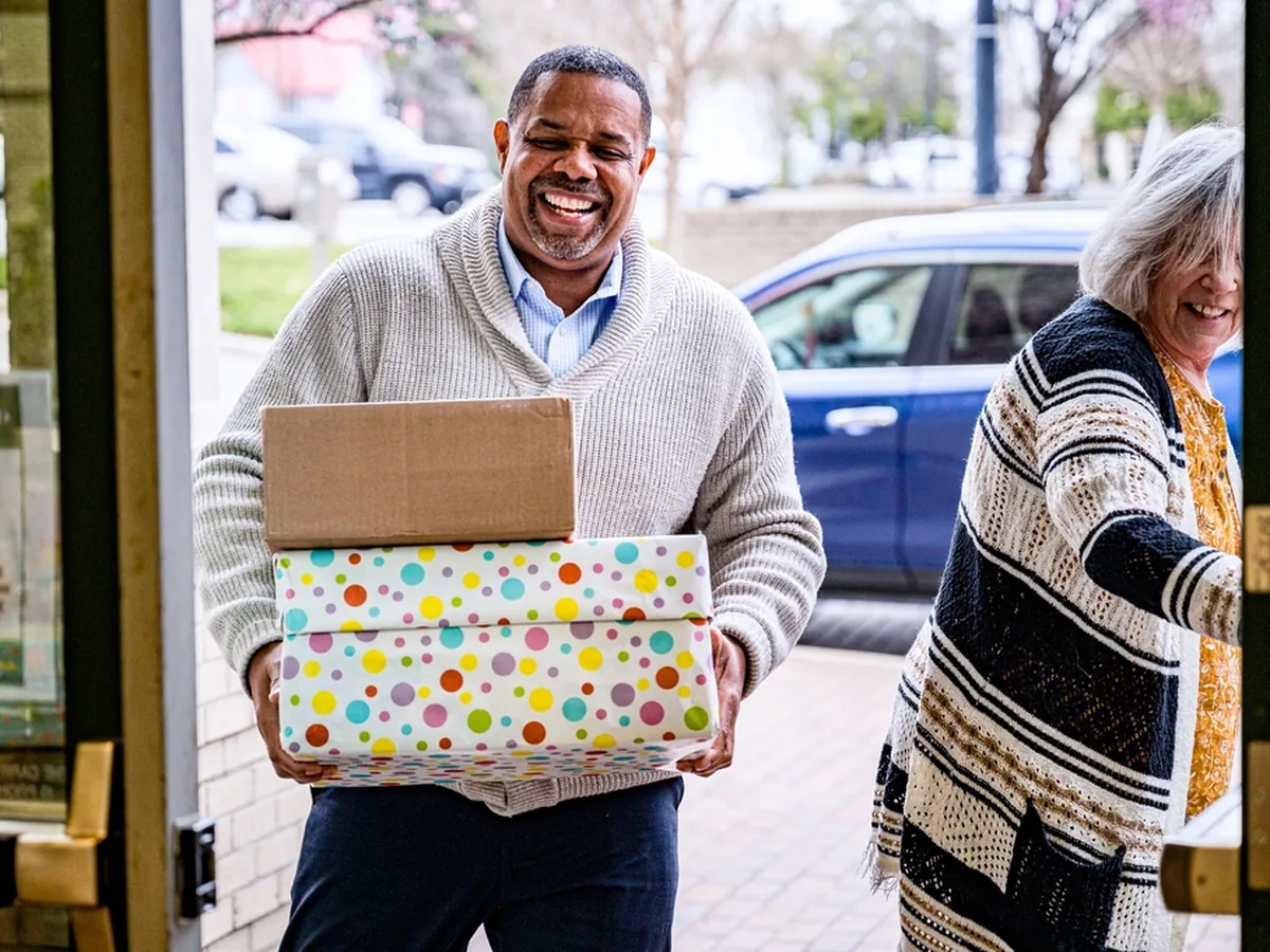 A smiling volunteer carries donated parcels through a doorway.