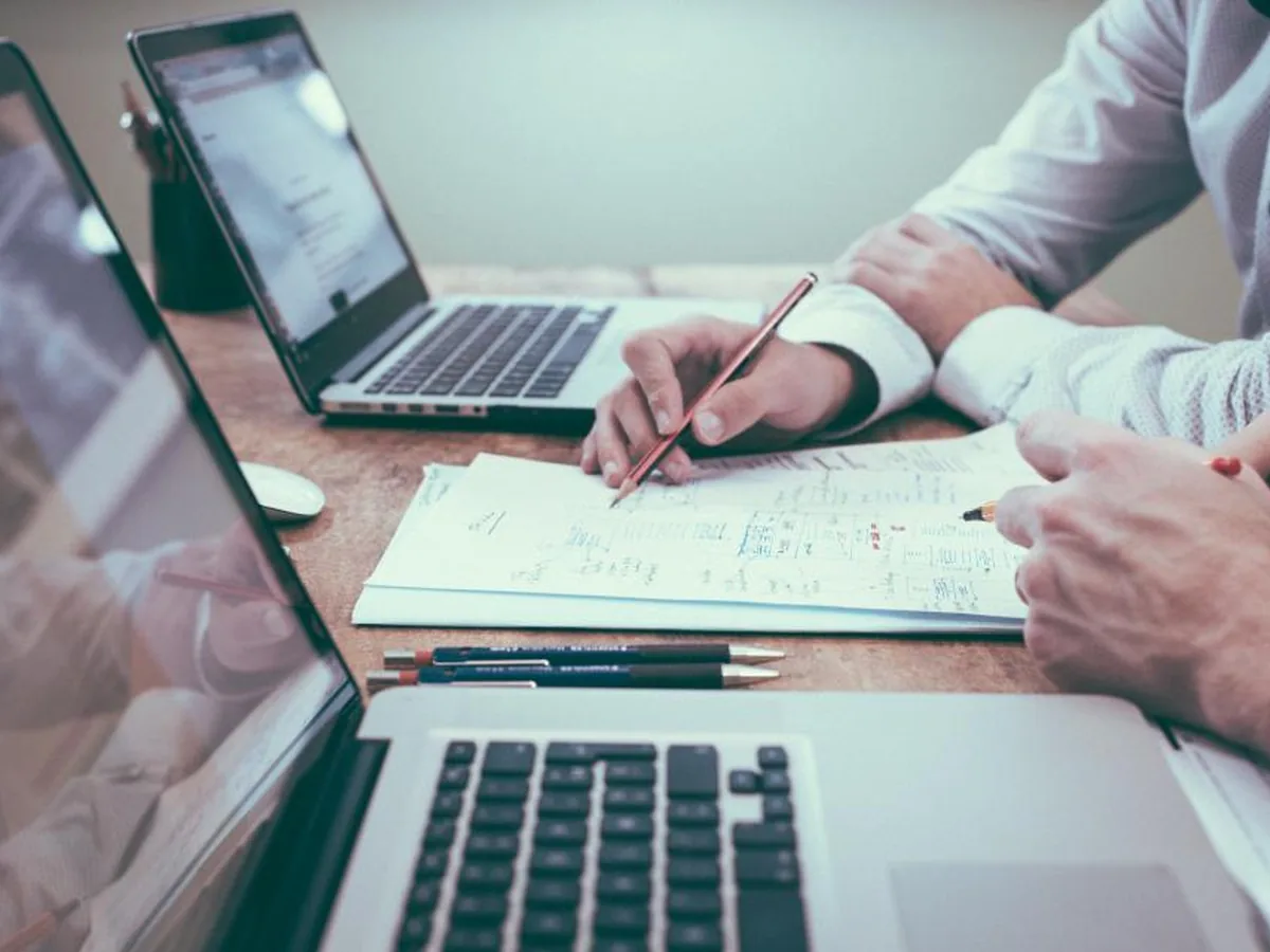 A professional reviews printed notes beside two laptops.