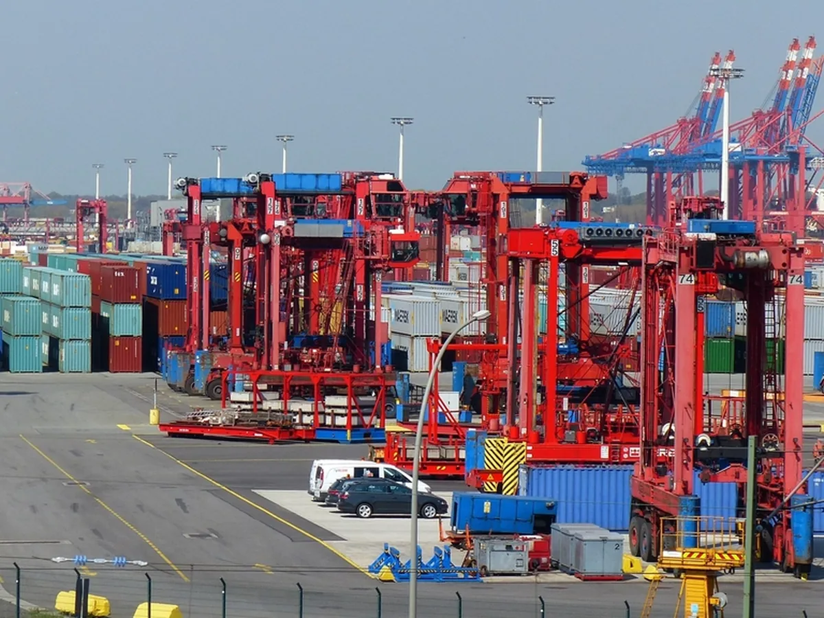 Container cranes and stacked shipping containers at a port terminal.